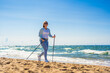 Nordic walking - mid-adult beautiful woman exercising on beach using  Nordic walking poles
