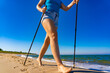 Nordic walking - mid-adult beautiful woman exercising on beach using  Nordic walking poles
