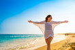 Beautiful woman with arms raised and outstretched walking on sunny beach
