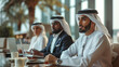 Arab businessmen in traditional attire engaged in a serious meeting, working on laptops in a modern office setting