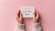 A kid hand holding a mini note written I love you mom against a clean pink backdrop with a big space for banner or product background, Generative AI.