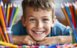Young boy smiling while drawing with colorful pencils.