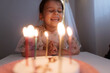 Happy child looks at a cake with candles. girl makes wishes, dreams or prays. celebrates birthday.