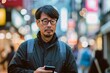 © anatolir - Adult man looks thoughtful while holding a smartphone on a brightly lit city street at night