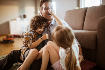 Wall Mural - Happy father playing with son and daughter at home