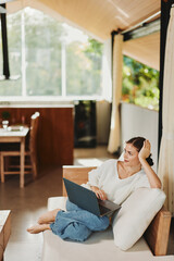 Wall Mural - Happy Woman Working from Home on Laptop in Cozy Living Room, Enjoying Online Business Success Young Freelancer Smiling in Modern Home Office, Using Wireless Technology for Communication and Online