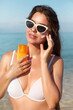 Beautiful young woman with sun cream on face. Girl holding sunscreen bottle on the beach and applying moisturizing lotion on skin.Skin care. Sun protection. Suntan