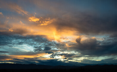 Dramatic sunset scene. The sky is filled with clouds and the sun is setting. The sky is full of clouds with a mix of blue and orange.