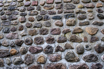 View of a wall made of various round and oval stones cemented into place.