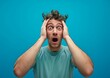 © Qstock - Shocked Young Man with Hands on Head Over Blue Background