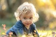 © anatolir - Adorable curly-haired toddler joyfully exploring the autumn nature in the park during the golden hour. Surrounded by falling leaves. Enjoying the bright sunlight and carefree outdoor play