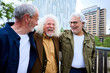 © CarlosBarquero - Group of three mature caucasian men enjoying embracing walk together laughing outdoor. Senior male old friends having fun hugging strolling happy in the urban city street. Elderly people golden ager