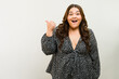 Joyful plus-size woman radiating confidence and pointing towards copy space in a studio
