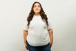 T-shirt mockup of a plus-size woman standing proudly in a studio, wearing a white shirt