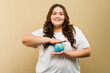 Smiling plus-size woman in a casual outfit holding a small globe in a studio setting