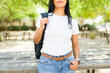 Young latina woman wearing a plain white t-shirt suitable for mockups, stands outdoors casually holding her shoulder bag strap