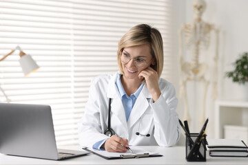 Canvas Print - Smiling doctor with laptop having online consultation at table in office