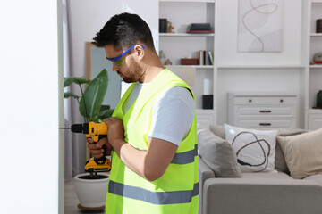 Wall Mural - Young worker in uniform using electric drill indoors