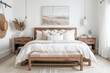 A modern farmhouse bedroom with white walls, light wood furniture, and neutral decor, featuring an oak bed frame, a bench at the foot, two nightstands on either side, a hanging pendant lamp above.