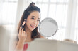 Attractive Asian Korean Female model using makeup brush and looking at makeup mirror at home. Skin care, Beauty face, Hairstyle.