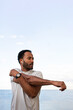 Vertical portrait of African American man stretching arm, warming up before workout and running outdoors. Copy space.