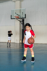 basketball by asian child or kid girl fun playing and training to learning bouncing and raising ball by left hand with children at sports stadium school or basketball court for exercise sport holiday