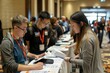 © Ilia Nesolenyi - Attendees checking in at a conference registration table with a group of people standing around