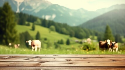 Wall Mural - Wooden table foreground with alpine meadow and cows with mountain backdrop. Rural life and eco-tourism concept. Cow walking and eating grass at animal farm with green mountain and blue sky. AIG35.