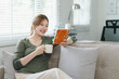 Young woman enjoying a relaxing morning with coffee and book on cozy couch at home. Work life balance concept
