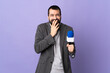 Adult reporter man with beard holding a microphone over isolated purple background happy and smiling covering mouth with hands