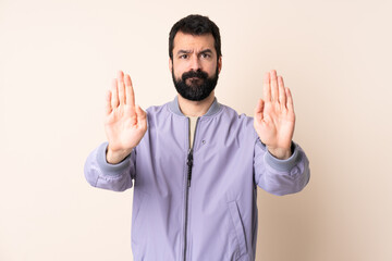 Wall Mural - Caucasian man with beard wearing a jacket over isolated background making stop gesture and disappointed