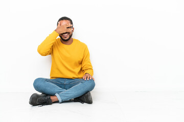 Poster - Young Ecuadorian man sitting on the floor isolated on white wall covering eyes by hands and smiling