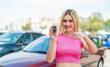 Young pretty blonde woman holding car keys at outdoors points finger at you with a confident expression