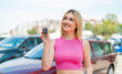 Young pretty blonde woman holding car keys at outdoors looking up while smiling