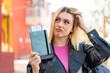 Young pretty blonde woman at outdoors holding a passport and having doubts