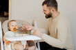 Father feeding italy pasta with tomato to baby boy at dining high chair