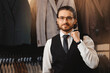 Portrait man in glasses in classic vest puts on suit jacket in shop store clothes for men.