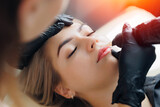 Fototapeta  - Permanent makeup artist at work tattoo for red lips for woman in beauty salon