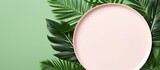 Fototapeta Dinusie - A minimalistic top down view of millennial pink paper background with an empty plate placeholder surrounded by vibrant green tropical palm leaves Perfect for your text or design ideas A visually appe