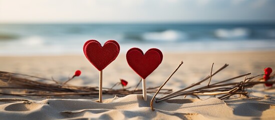 Poster - Two heart shaped cutouts in vibrant red color are attached to the tops of sticks creating a lovely and romantic picture against the backdrop of a sandy beach with an unoccupied area for additional im