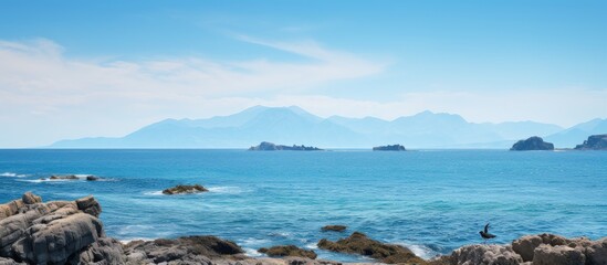 Aufkleber - A stunning seascape featuring a rocky mountain in the foreground with a bird gracefully perched in front The background showcases a mesmerizing expanse of deep blue ocean providing the perfect space
