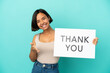 © luismolinero - Young mixed race woman isolated on blue background holding a placard with text THANK YOU making a deal
