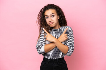 Wall Mural - Young hispanic woman isolated on pink background pointing to the laterals having doubts