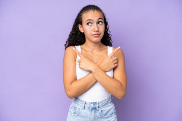 Wall Mural - Young woman isolated on purple background pointing to the laterals having doubts