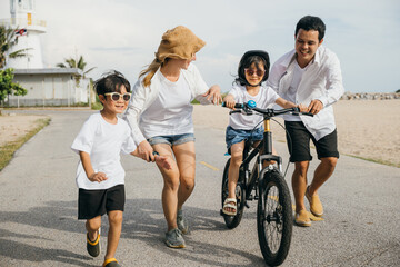 Wall Mural - A heartwarming family moment unfolds on a sandy beach as parents teach their children joy of bicycle riding. Smiles balance and warmth of sun create a cheerful and unforgettable summer scene.