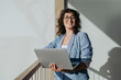 Cheerful businesswoman standing with a laptop on a balcony