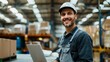 © iuricazac - Smiling man in hard hat and apron sitting at a desk with a laptop in a warehouse setting.