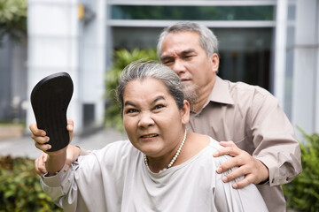 Angry old senior woman holding slipper and being ready to slap or hurt you, concept image of violence, aggression, physical assault, anger management with other people trying to stop her