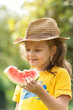 Little girl in a hat eats a ripe red watermelon