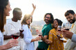 © CarlosBarquero - Happy international community enjoying party dance with glass of red wine at sunset rooftop party. Girl dancing with raised hands at disco outdoors with friends. Beautiful people having fun together